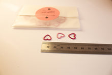 Load image into Gallery viewer, Heart-shaped stitch markers on a white surface with a ruler for scale.