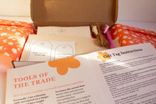 Load image into Gallery viewer, Open kit with fabric, twine, instructions, and fabric pen on a patterned tissue
