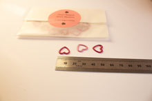 Load image into Gallery viewer, Heart-shaped stitch markers on a white surface with a ruler for scale.
